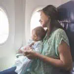 Happy mother and baby sitting together in airplane cabin near window