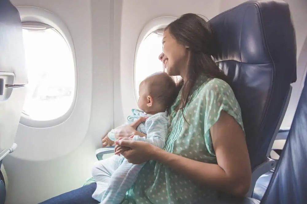Happy mother and baby sitting together in airplane cabin near window