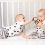 two twin babies play in the crib