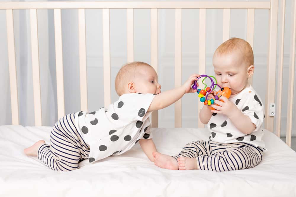 two twin babies play in the crib