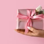 emale hand with beautiful gift box on color background, closeup