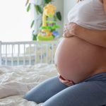Young beautiful pregnant woman, sitting on bed in bedroom