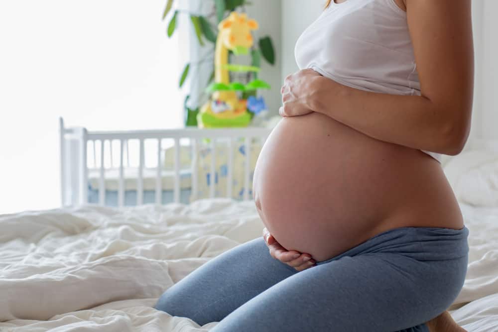 Young beautiful pregnant woman, sitting on bed in bedroom