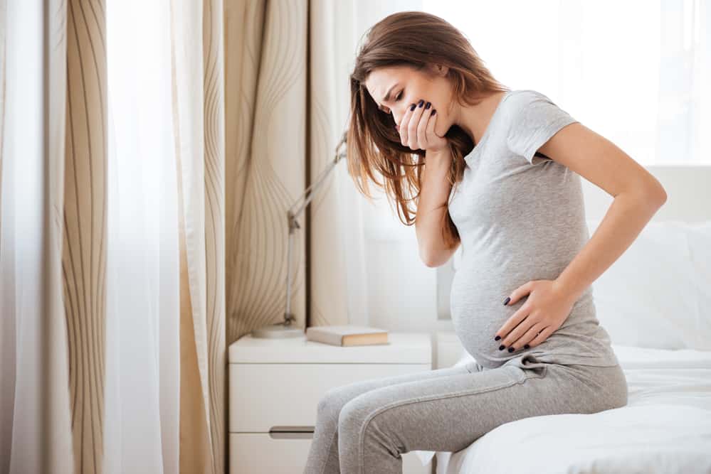 Pregnant young woman sitting on bed and feeling sick