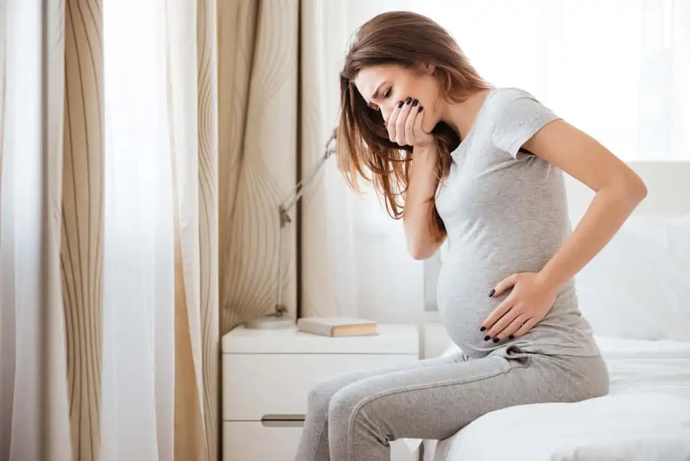 Pregnant young woman sitting on bed and feeling sick