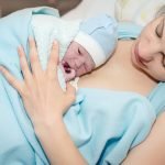 Young beautiful woman with a newborn baby after birth wearing robe