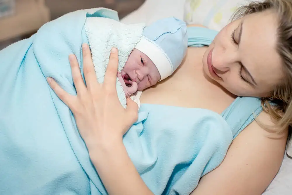 Young beautiful woman with a newborn baby after birth wearing robe